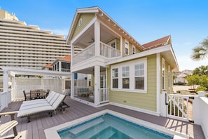 A two-story house with a balcony, a pool, and a deck with lounge chairs.