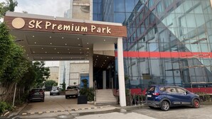 La entrada al SK Premium Park, con una fachada de vidrio moderna y un área de acceso cubierta.