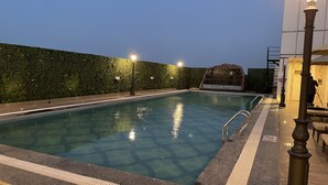 Una piscina con una fuente de agua cristalina azul, rodeada por un seto y un muro de piedra.
