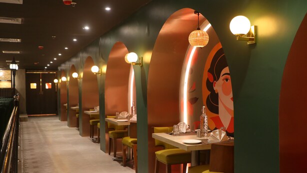 Un restaurante con mesas y sillas, una barra alargada y una pared con un mural.