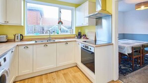 A compact kitchen with white cabinets, a built-in oven, and a window with a view of a house. - Host & Stay | St Mark's Close (Marske-by-the-Sea)