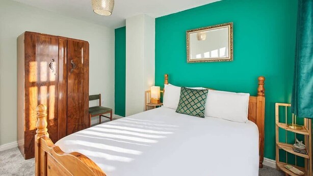 A bedroom with a wooden bed, a green wall, a mirror, and a wardrobe. - Host & Stay | St Mark's Close (Marske-by-the-Sea)