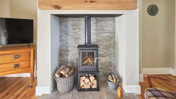 Ein Kaminofen mit Holzscheiten, ein Fernseher und ein Holzkabinett in einem Wohnzimmer.