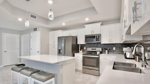 A modern kitchen with white cabinetry, stainless steel appliances, and a central island with bar stools. - 3121-108 Resort Lake View Disney Universal Orlando (Kissimmee)