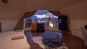 Een tentaccomodatie met een bed, een ronde tafel en uitzicht op de omgeving.