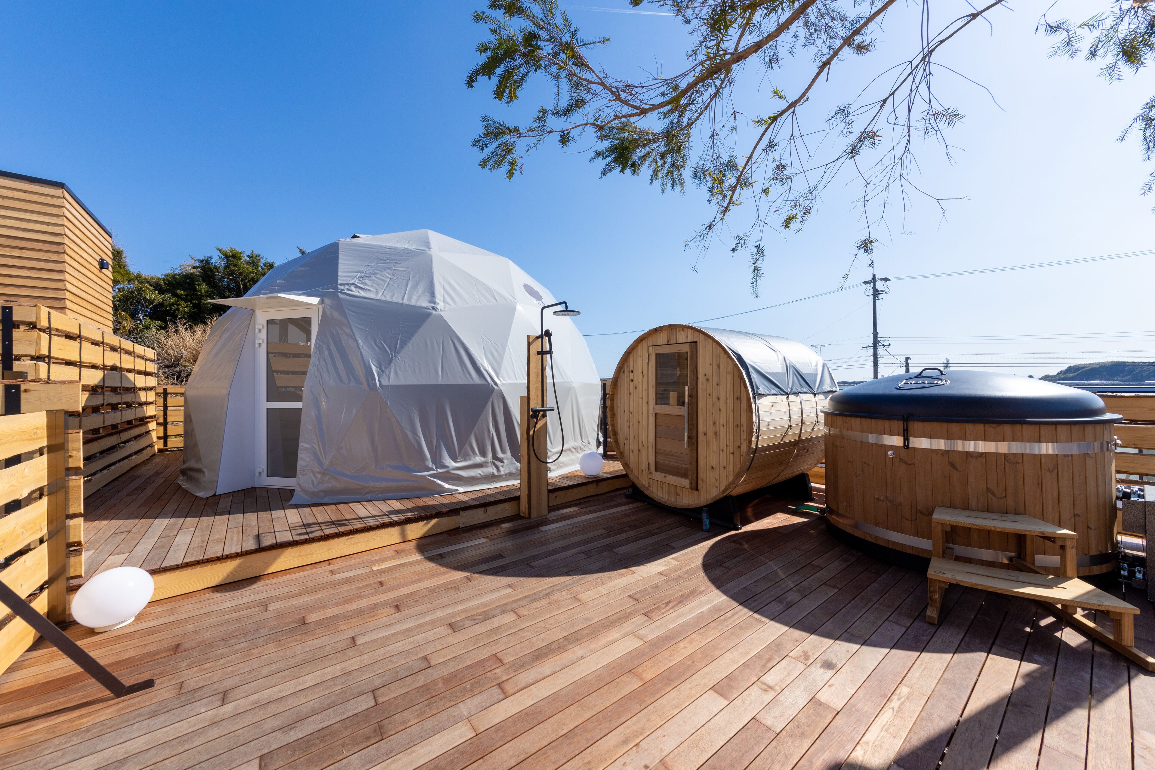 Une terrasse en bois avec un sauna, un espace de couchage abrité et un chalet en bois.
