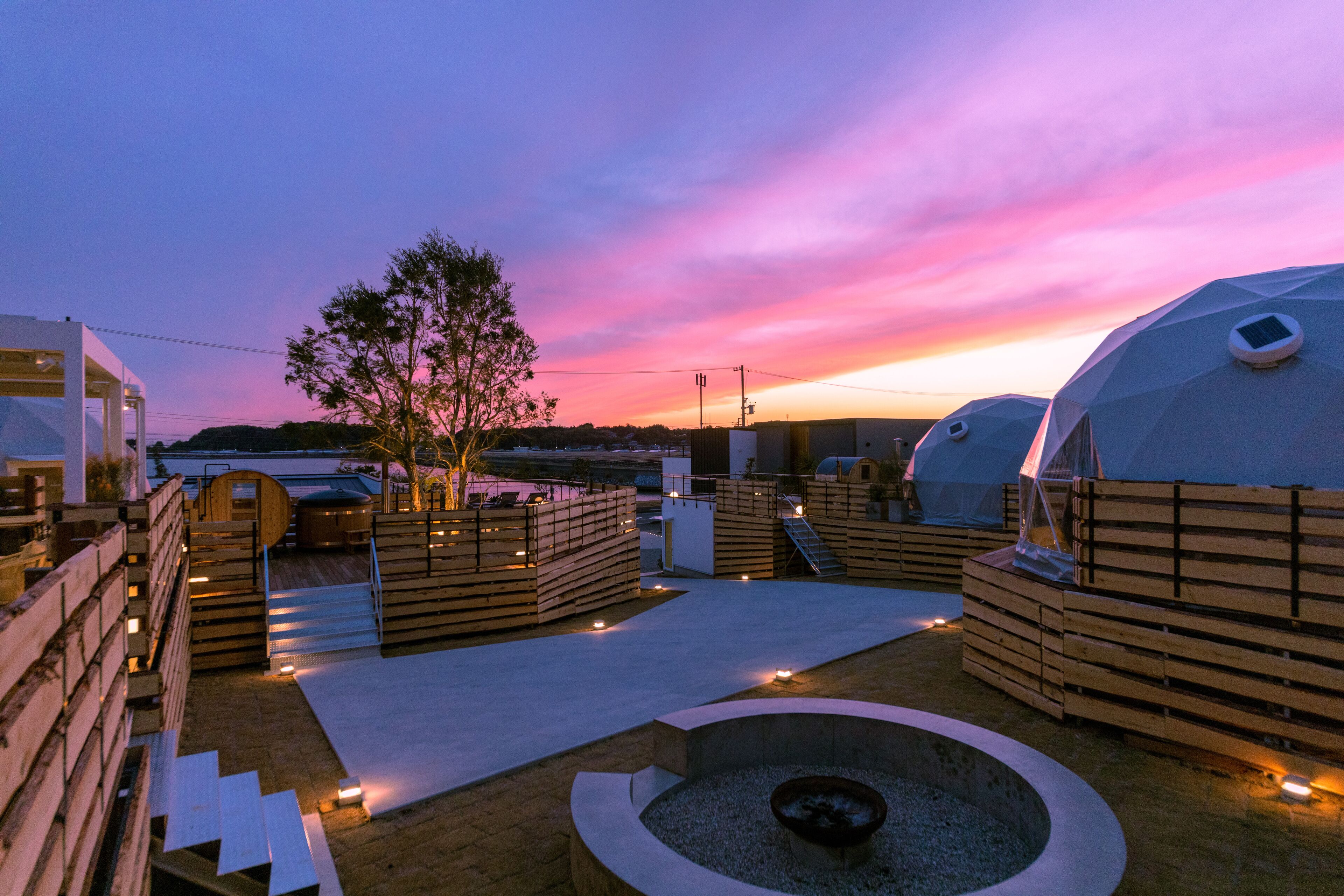 Una azotea con zonas de estar de madera, un hogar y vistas al atardecer.