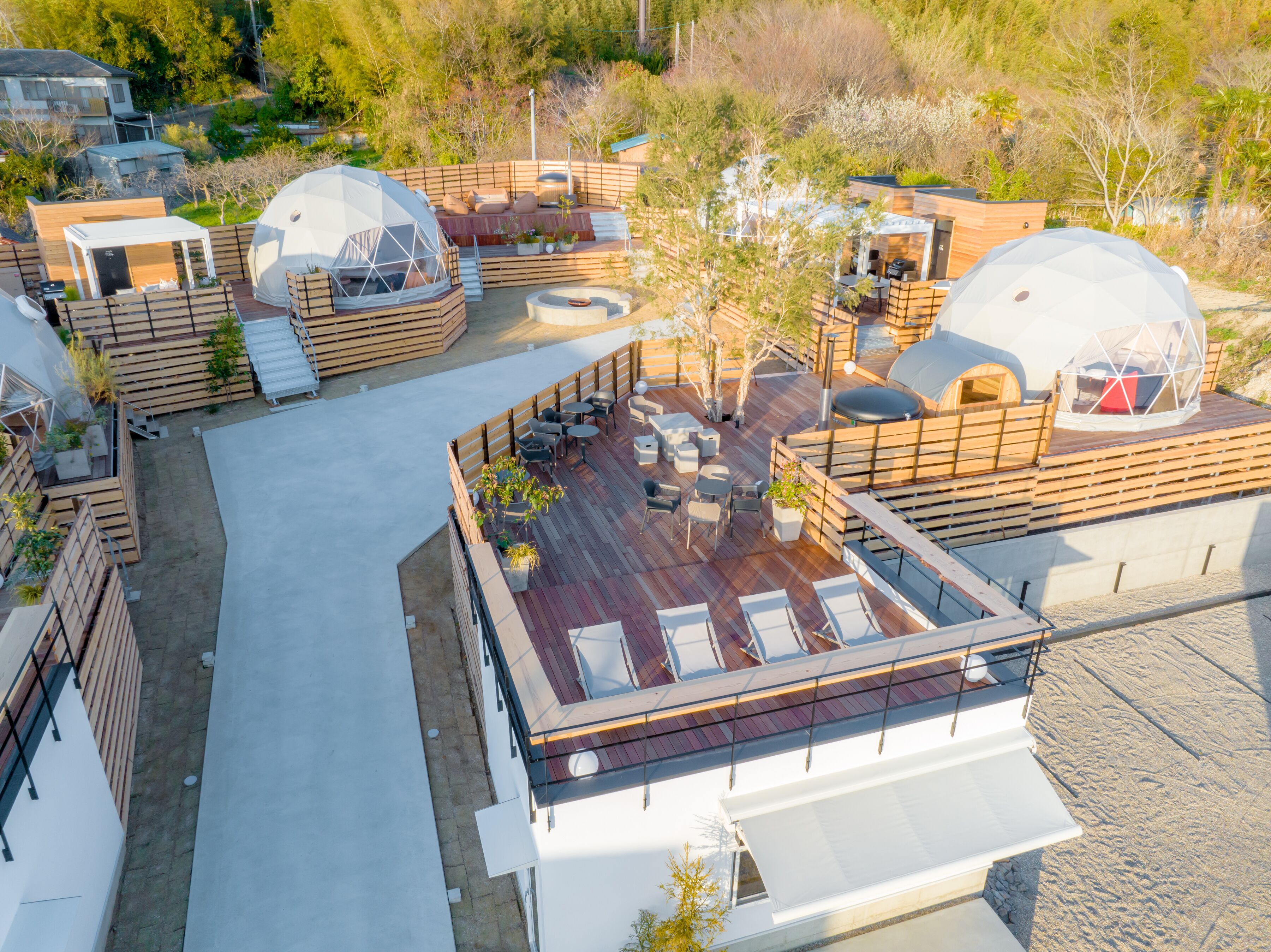 A rooftop terrace with multiple seating areas, including a sun lounge and a dining area, surrounded by wooden railings and potted plants.