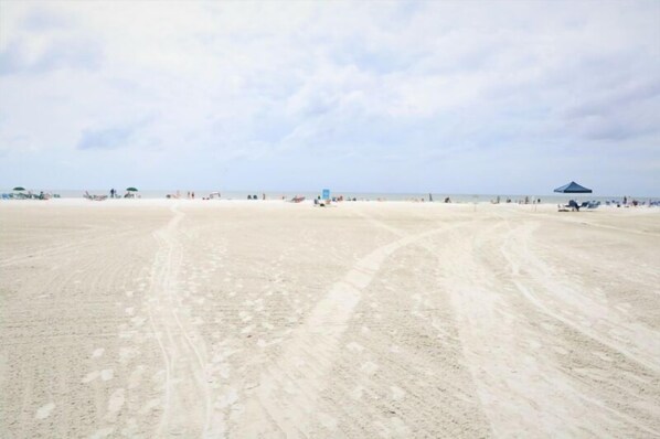 Una extensa playa arenosa con huellas y algunas sombrillas de playa.
