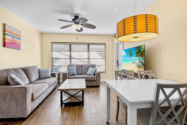 A living room with a sofa, a coffee table, a dining table, and a ceiling fan.