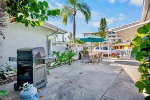 A patio area with a grill, outdoor furniture, and a white fence.