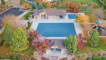An aerial view of a property with a large rectangular swimming pool, a covered patio area, and a small building with a garage.