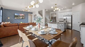 Une cuisine moderne avec des meubles blancs, un réfrigérateur en acier inoxydable et un coin repas agrémenté d’une table en bois, mise pour quatre personnes.