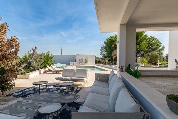 A modern outdoor living area with a pool, lounge chairs, and a covered seating area.