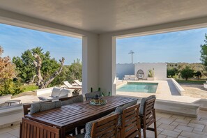 A covered outdoor area with a pool, seating, and a view of the landscape.