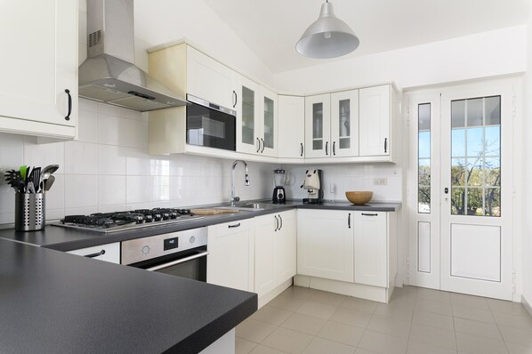 A modern kitchen with white cabinets, a gas stove, and a coffee maker.