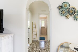A hallway leading to a bathroom with a shower, a ladder, and decorative plates on the wall.