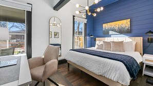 A modern bedroom with a large bed, a desk, and a chair. There is a window with a view of the outside. - Old Town Retreat w/ Hot Tub Steps From Csu! (Fort Collins)