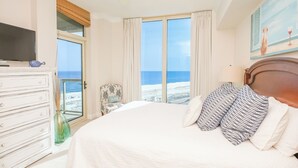 A bedroom with a large bed, a dresser, a television, and a view of the beach. - 2B Stunning Sunset Views P3-1003 (Pensacola Beach)