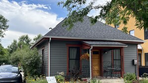 A two-story house with a grey exterior, a red front door, and a small porch with outdoor furniture. - Lavish Retreat in Old Town - Walk Everywhere! (Fort Collins)