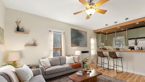 A modern living room with a sofa, coffee table, and a kitchen area with bar stools. - Lavish Retreat in Old Town - Walk Everywhere! (Fort Collins)