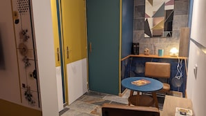Une pièce avec une porte bleue et jaune, une table ronde sur laquelle se trouve un livre, et une chaise.