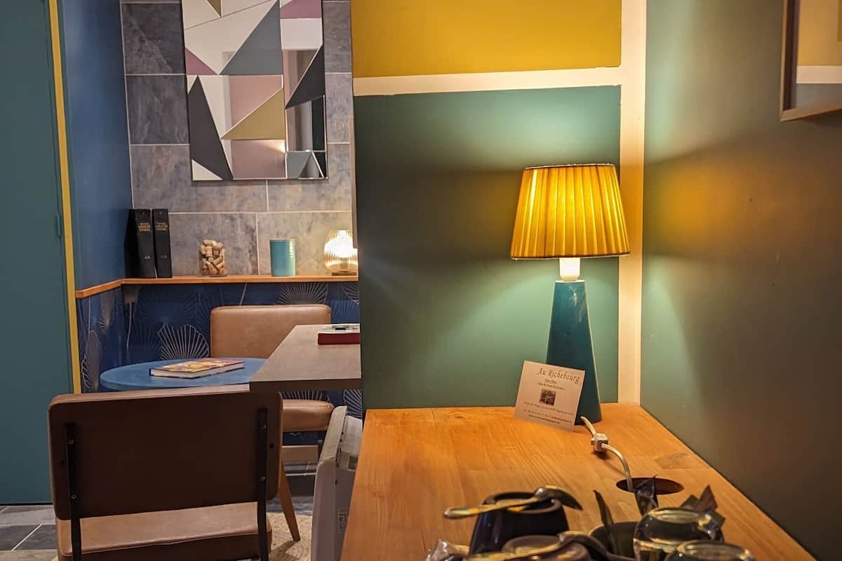 Une chambre d’hôtel avec une table à manger en bois, une chaise, une lampe et un plateau sur lequel se trouvent une théière et des verres.