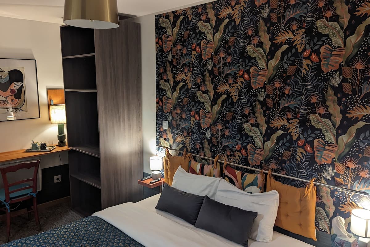 Une chambre d’hôtel avec un lit, un bureau, une chaise, une lampe et un grand tableau abstrait accroché au mur.