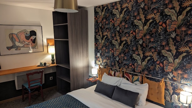 Une chambre d’hôtel avec un lit, un bureau, une chaise, une lampe et un grand tableau abstrait accroché au mur.