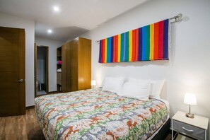 A bedroom with a bed, a nightstand, a lamp, a wardrobe, and a colorful striped curtain. - Modern 1BR | Walk to Beach & Boardwalk (Puerto Vallarta)
