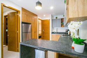 A modern kitchen with wooden cabinets, a stainless steel refrigerator, a granite countertop, and a potted orchid. - Modern 1BR | Walk to Beach & Boardwalk (Puerto Vallarta)