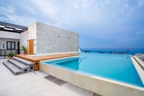 A modern outdoor pool area with a clear view of the ocean, a wooden deck, and a glass-enclosed structure. - Modern 1BR | Walk to Beach & Boardwalk (Puerto Vallarta)