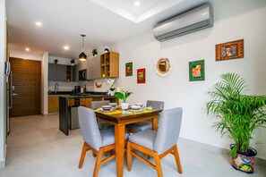 A modern kitchen with a dining area, featuring a wooden table, grey upholstered chairs, and a potted plant. - Modern 1BR | Walk to Beach & Boardwalk (Puerto Vallarta)
