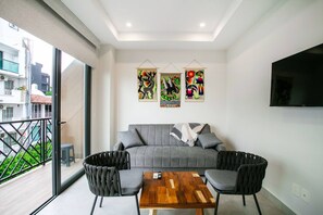 En moderne stue med en grå sofa, to lænestole og et træbord. Der hænger tre farverige billeder på væggen over sofaen.