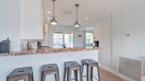 A kitchen with a marble countertop, three stools, pendant lights, and a view to the outside. - Pompano Oasis w/ Heated Pool 8 mins to the Beach! (Pompano Beach)