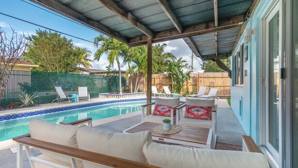 A covered outdoor area with a pool, lounge chairs, and a wooden bench. - Pompano Oasis w/ Heated Pool 8 mins to the Beach! (Pompano Beach)
