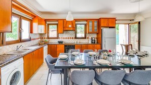 Una cocina moderna con armarios de madera, horno empotrado y comedor con mesa de vidrio para seis comensales.