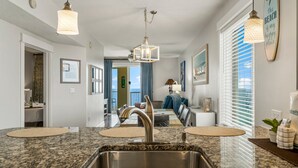 A kitchen with granite countertops, a stainless steel sink, pendant lights, and a dining area with a table and chairs.