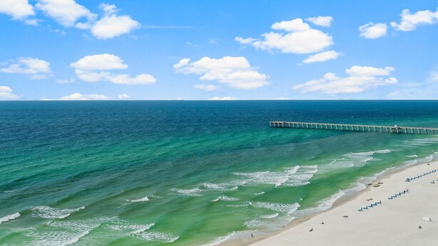 A beach with clear turquoise water, a sandy shore, and a pier extending into the ocean.