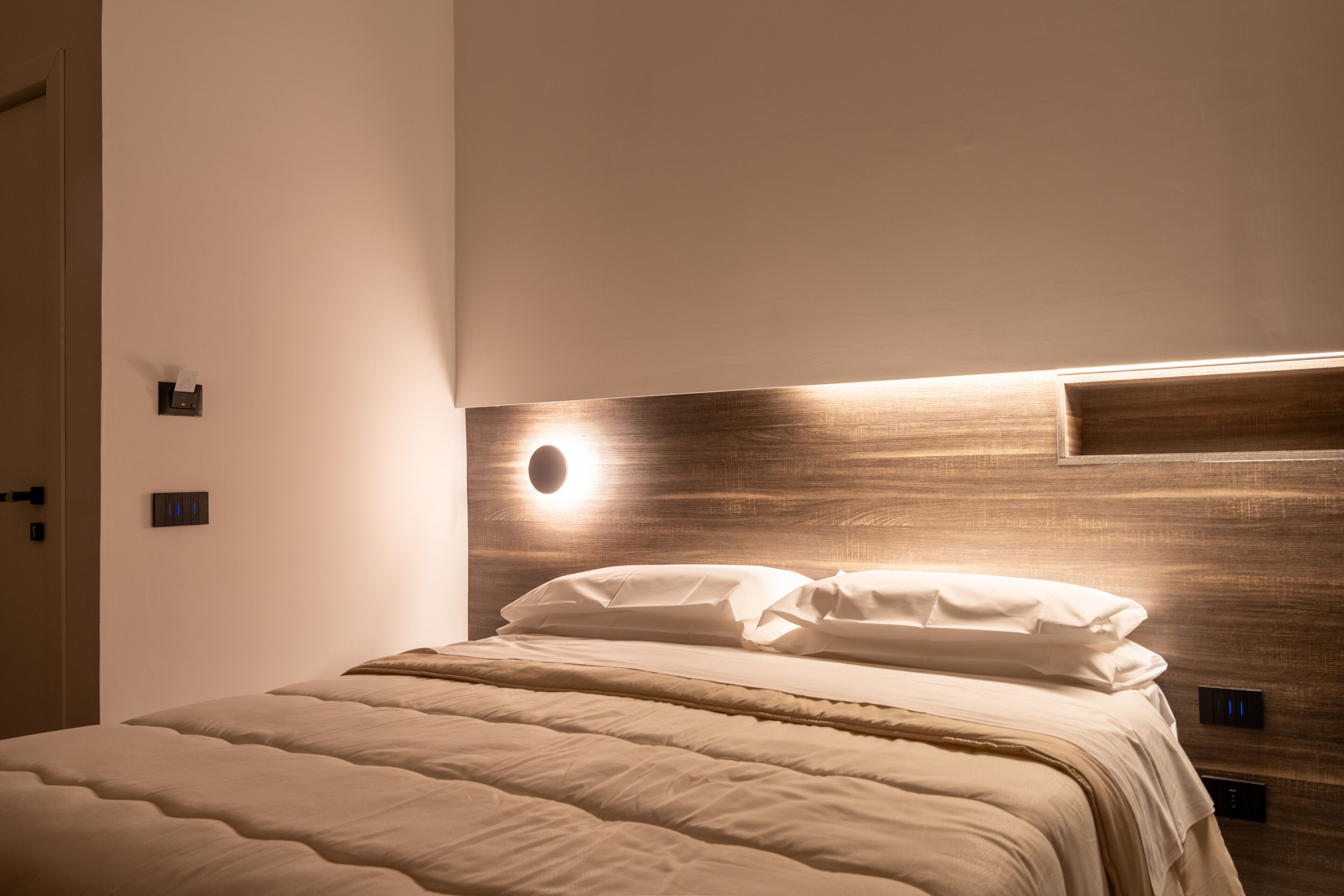 A neatly made bed with a wooden headboard and a wall-mounted light fixture.