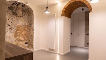 Un interior moderno con paredes de piedra vista, un mostrador de recepción de madera y un armario blanco bajo un arco de ladrillo.