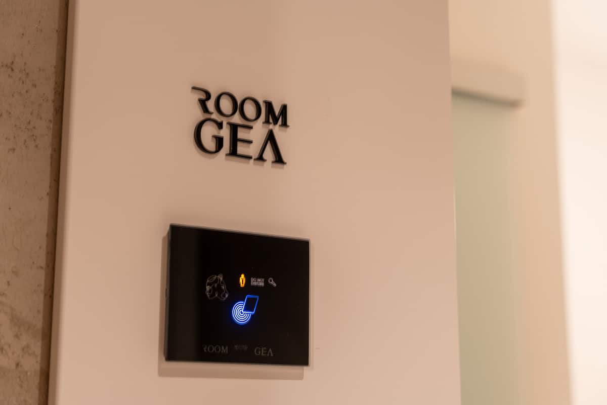 Ein an der Wand befestigtes Schild mit der Aufschrift „ROOM GEA“ und einer Bedienkonsole mit Symbolen.