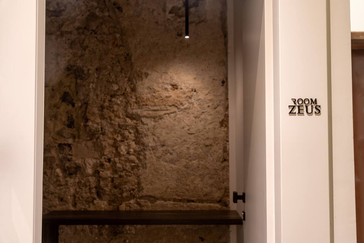 Eine strukturierte Steinwand mit einem Holzregal und einem Schild mit der Aufschrift 'ROOM ZEUS'.