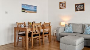 A dining area with a wooden table and chairs, a grey sofa with patterned cushions, and a small side table with a lamp. - Life's a Beach - Direct Beach Access, Sea Views (Saundersfoot)