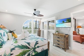 Una camera da letto con un letto, una televisione, un comò in vimini e vista sulla spiaggia.