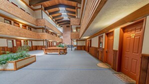 Un hall d’hôtel à plusieurs niveaux, avec des panneaux de bois, un espace salon central et un sol recouvert de moquette.