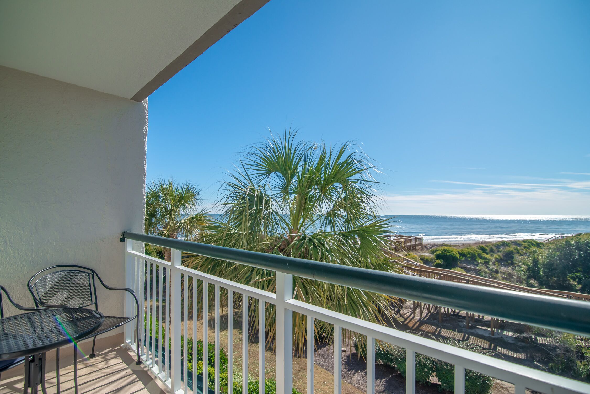 A balcony with a view of the ocean, palm trees, and a white railing.