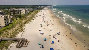 A beach with a wooden boardwalk leading to a building complex.