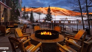 A fire pit with chairs around it, overlooking a snowy landscape with a mountain in the background.