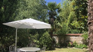 A patio with a round table and four chairs, surrounded by lush greenery and a stone wall. - Family home in the heart of the Eure valley - 10 people - 5 bedrooms (Breuilpont)